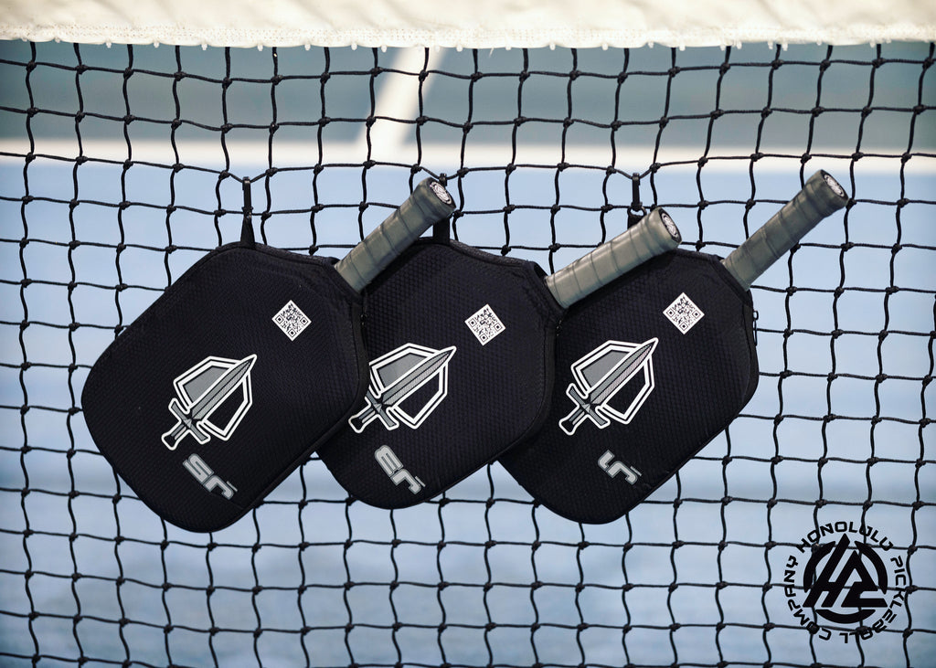 Honolulu Sword & Shield paddles in covers on a pickleball net
